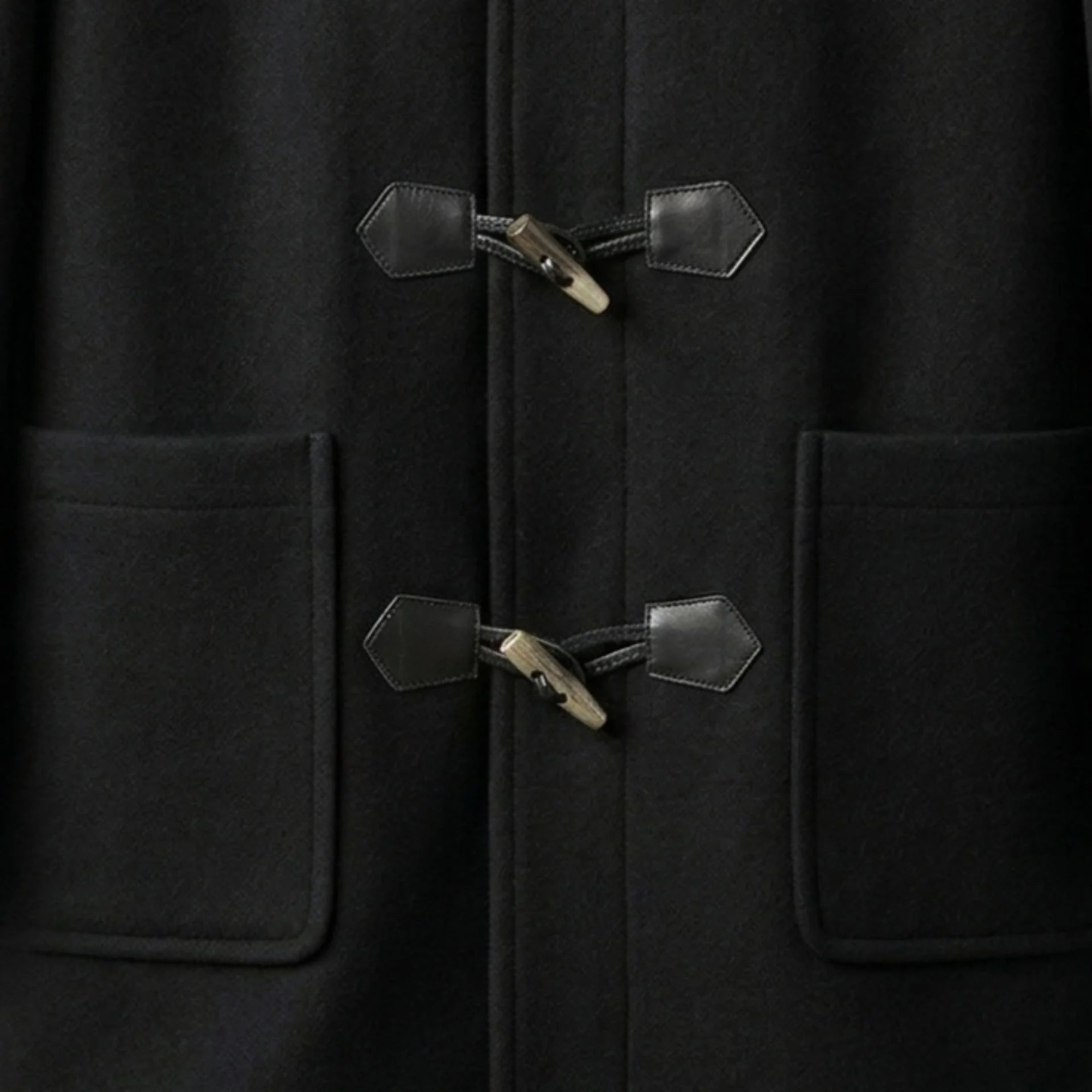 Close up of toggle fastenings and patch pockets on men's black hooded duffle coat.