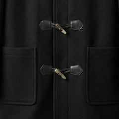 Close up of toggle fastenings and patch pockets on men's black hooded duffle coat.