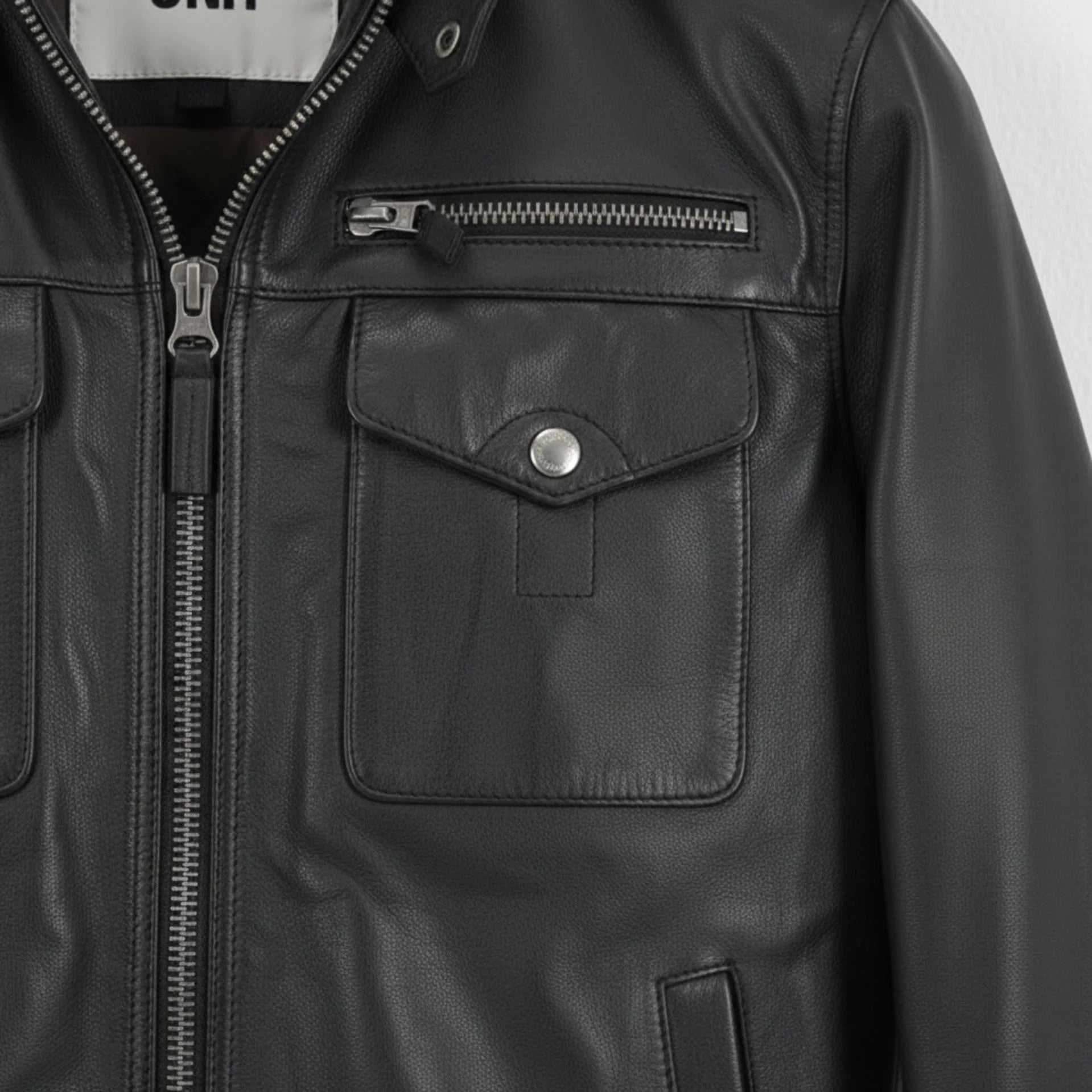 detail of chest flap pockets and zipper on men's black leather utility jacket.