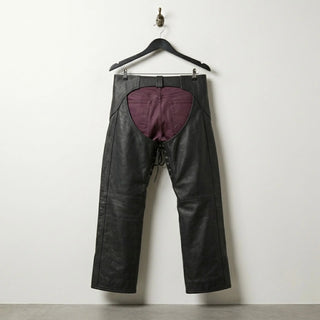 Back view of open back black leather motorcycle chaps worn over burgundy pants