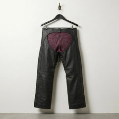 Back view of open back black leather motorcycle chaps worn over burgundy pants