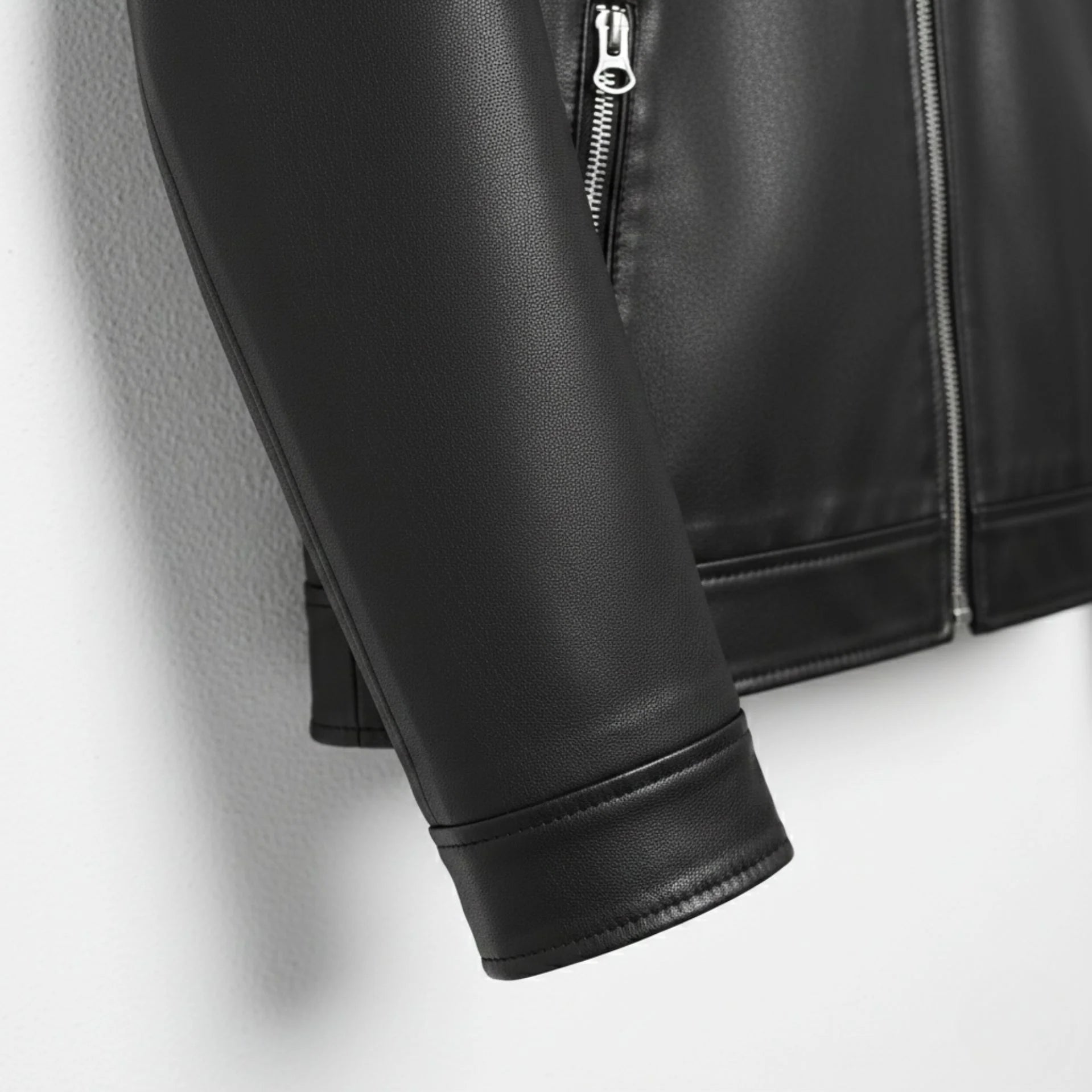 Detail of sleeve and cuff on men's black PU leather jacket with zip cuffs.