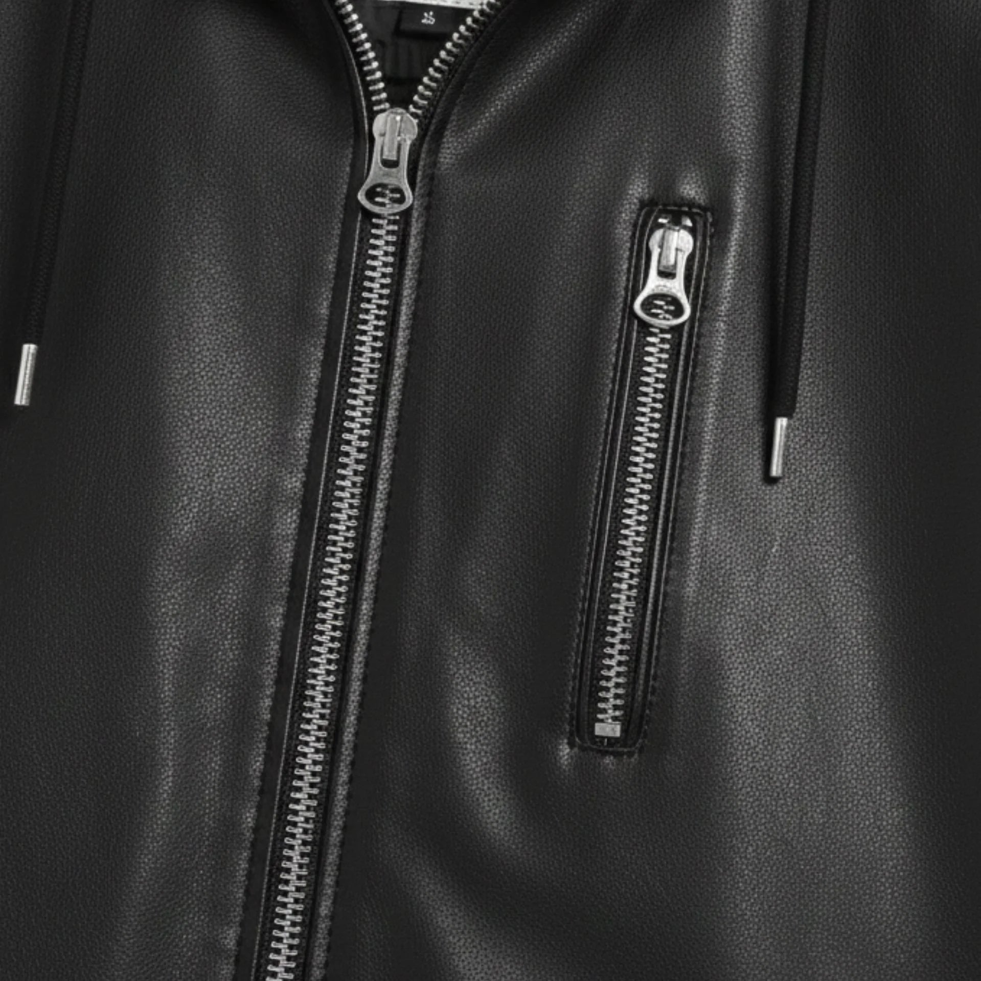 Close‑up of metal zippers on men's black hooded leather motorcycle jacket.