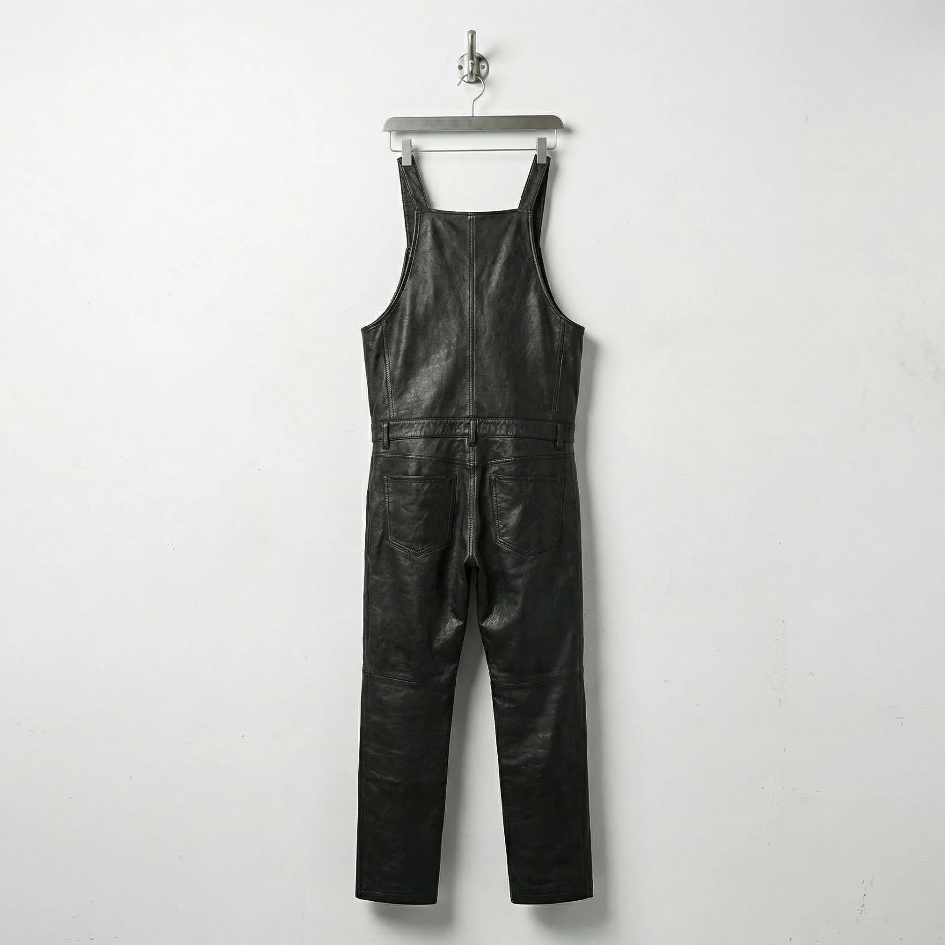 Back view of men's black leather bib overalls showing straight legs and back pockets
