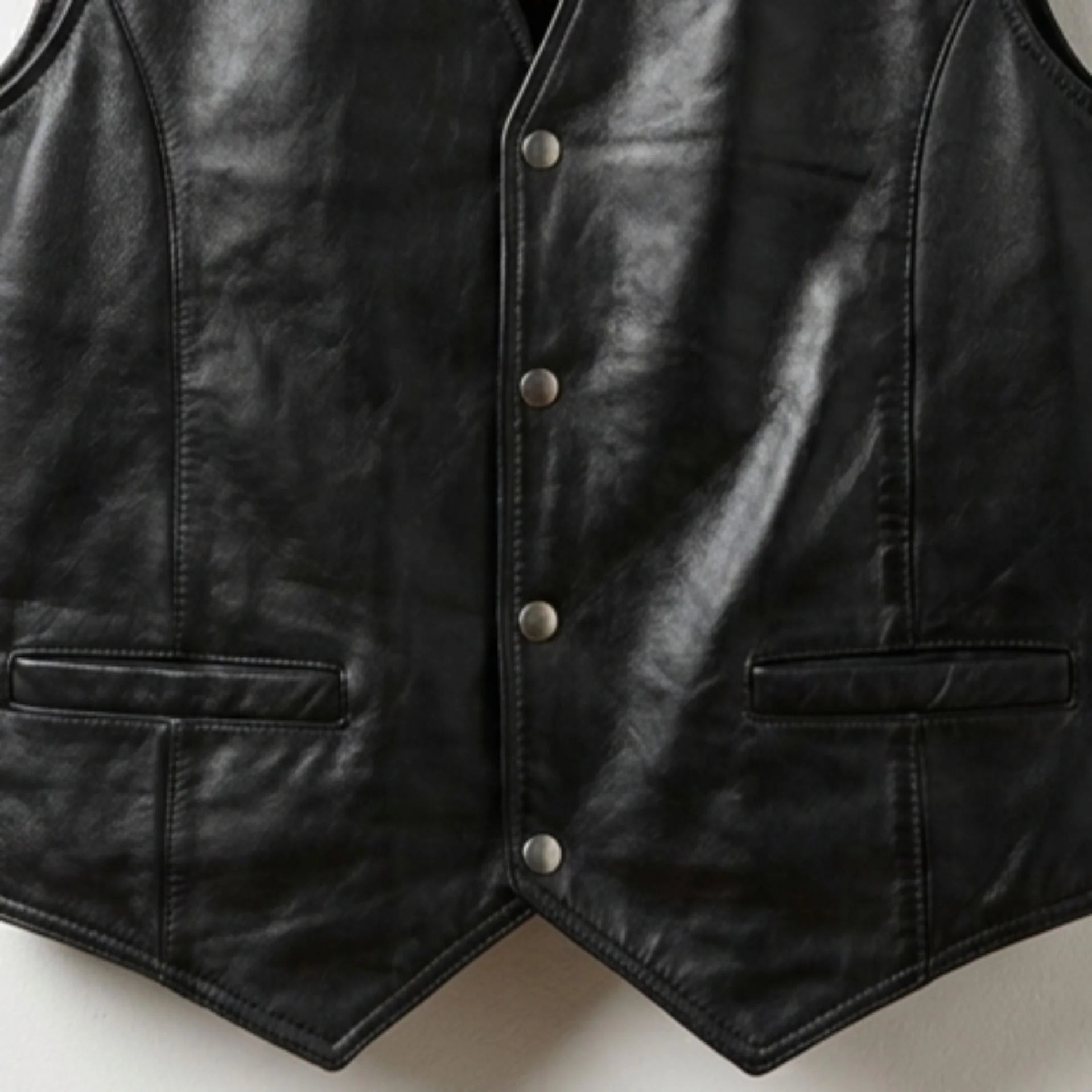 Close-up of snap buttons, welt pockets and pointed hem on men's black leather vest