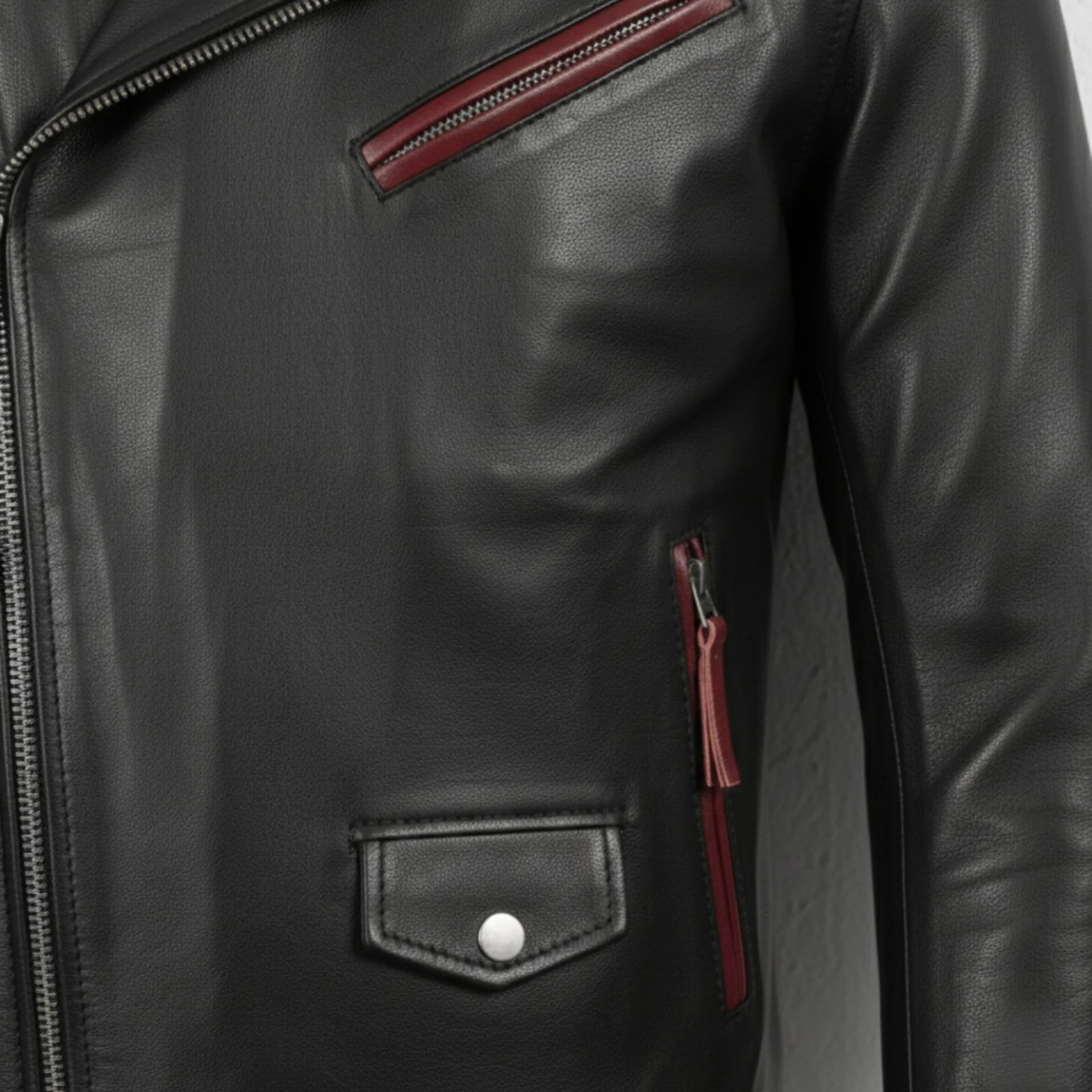 detail of zipper pockets and flap pocket on men's black and maroon leather jacket.