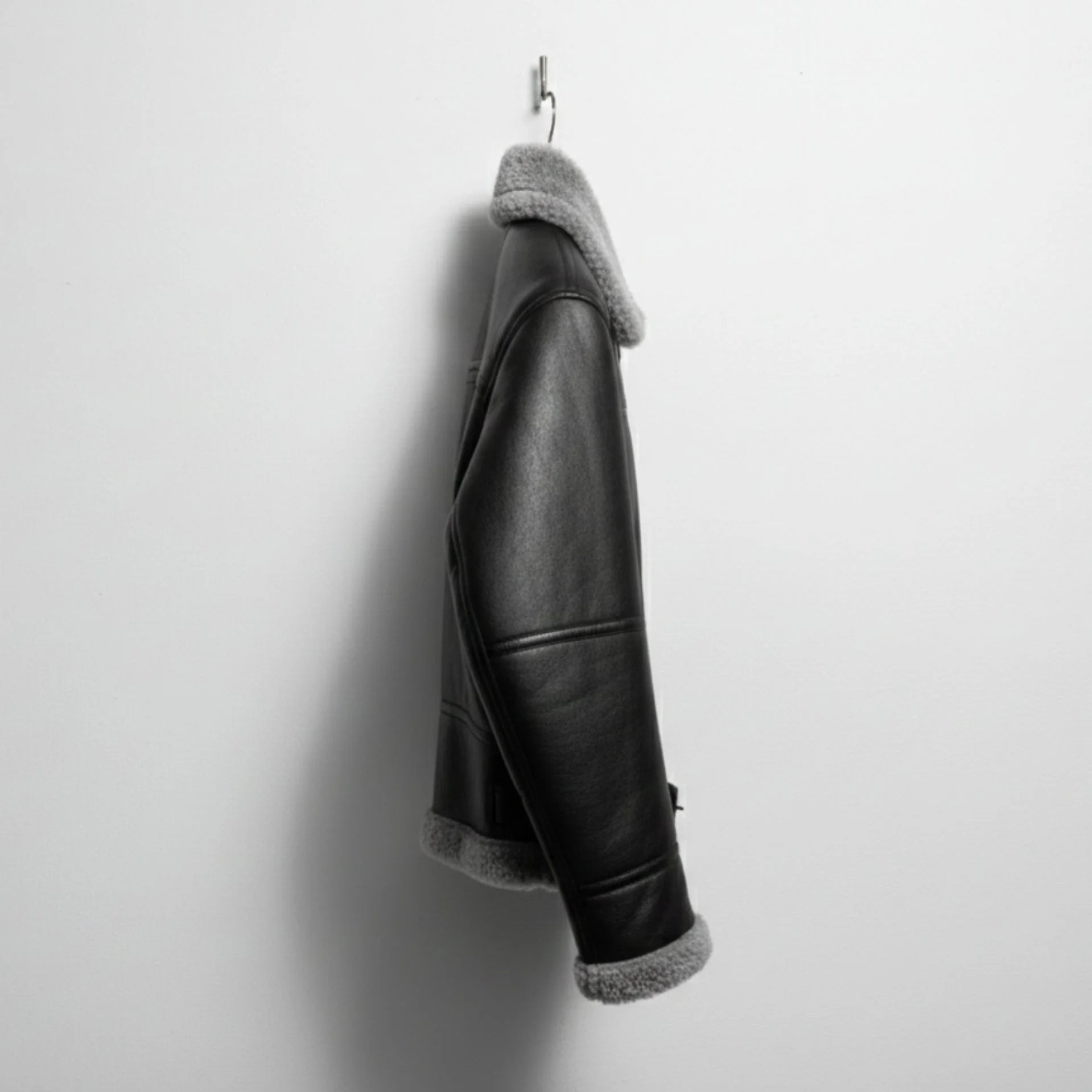 side profile mens black shearling bomber leather jacket hanging on wall.