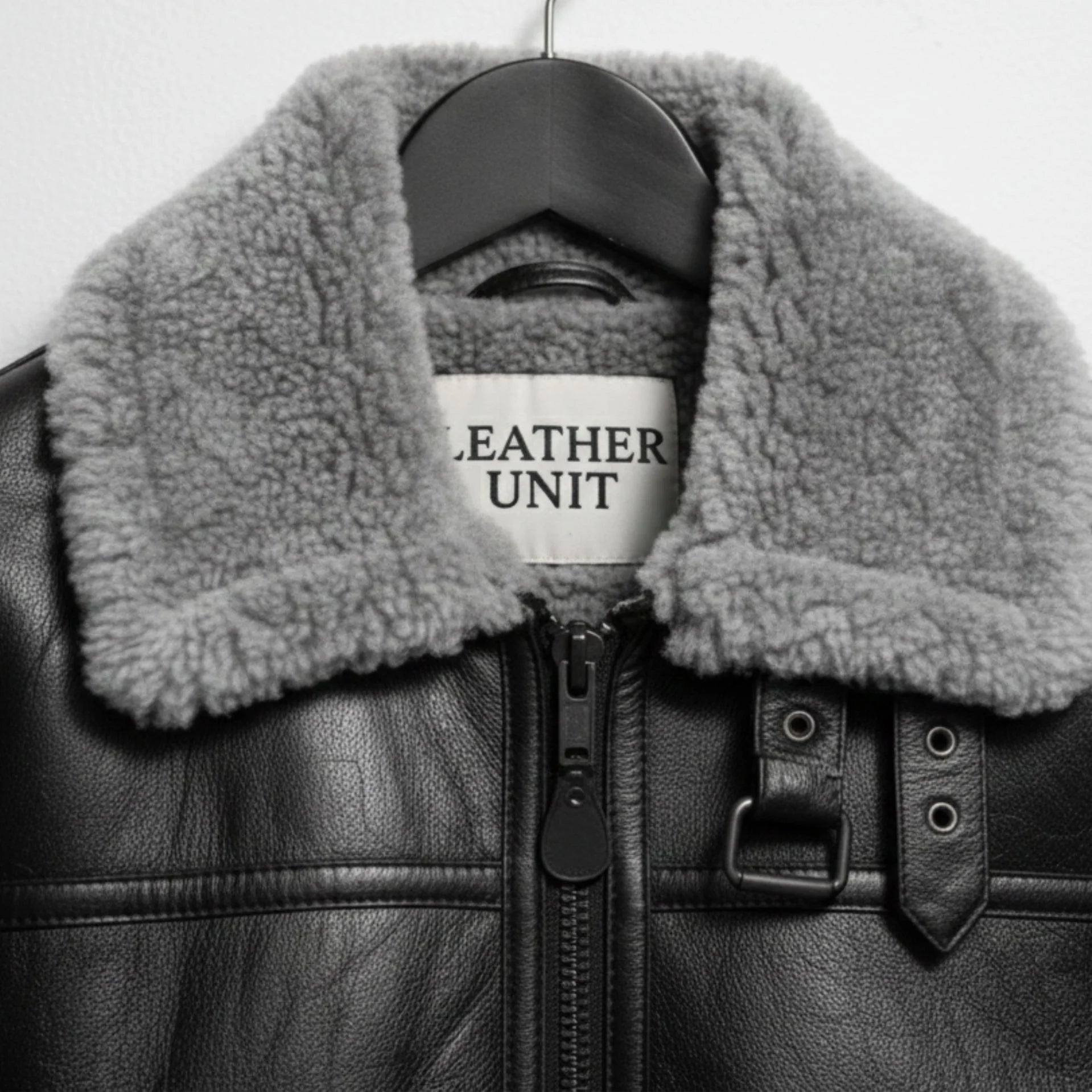 close up grey shearling collar and buckle throat latch on black leather jacket.