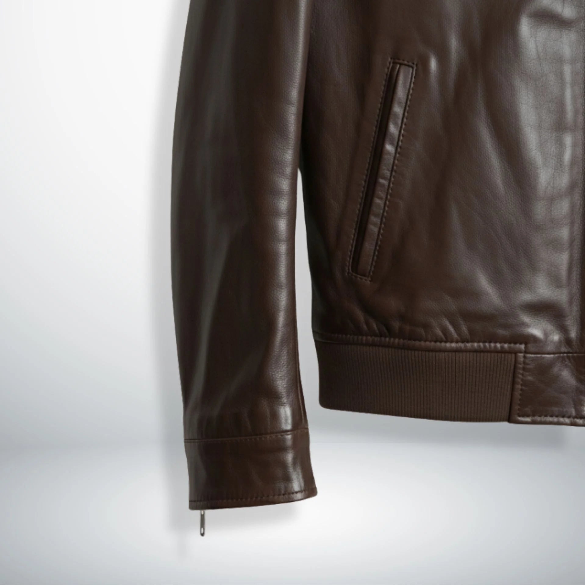 close up ribbed hem and pocket detail on brown leather bomber jacket.