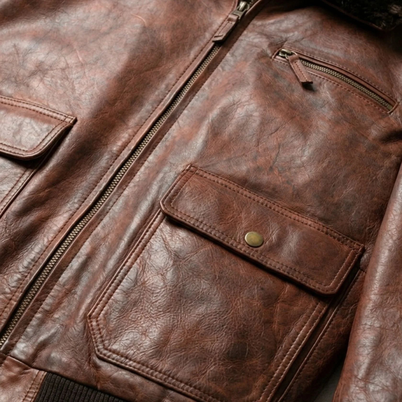 close up flap pockets zipper and grain on mens brown bomber leather jacket.