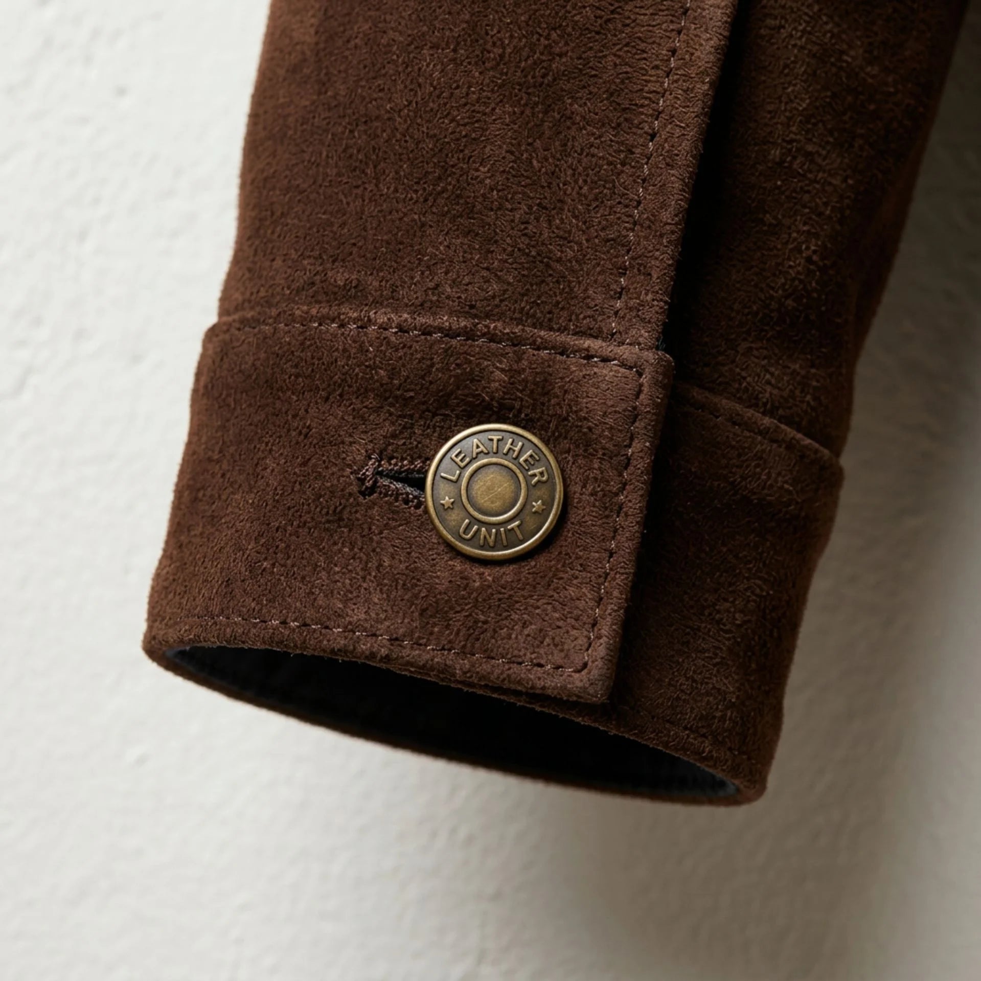 Detail of cuff with branded Leather Unit snap button on brown suede jacket.