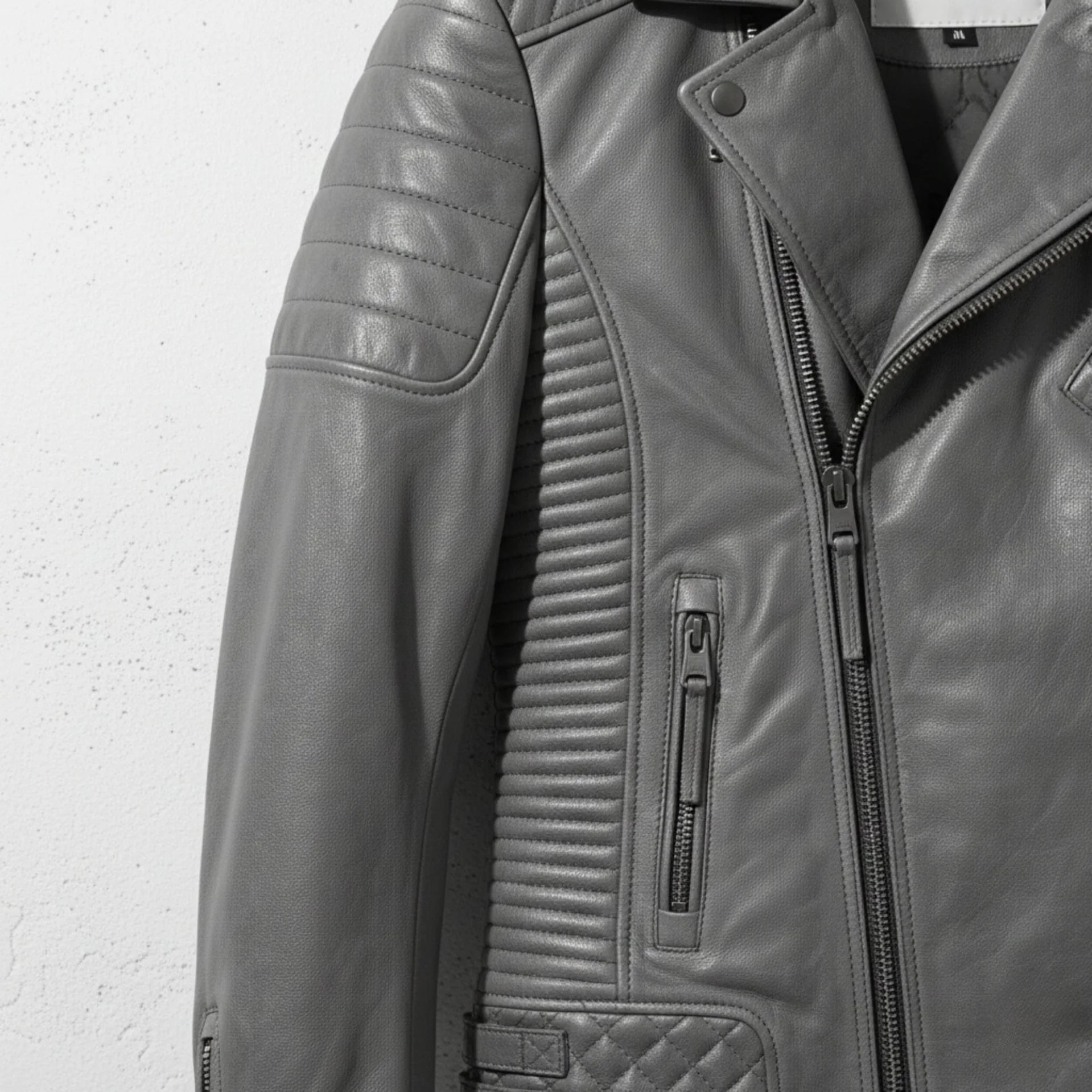 detail of ribbed side panel and zipper pocket on men's grey quilted moto jacket.