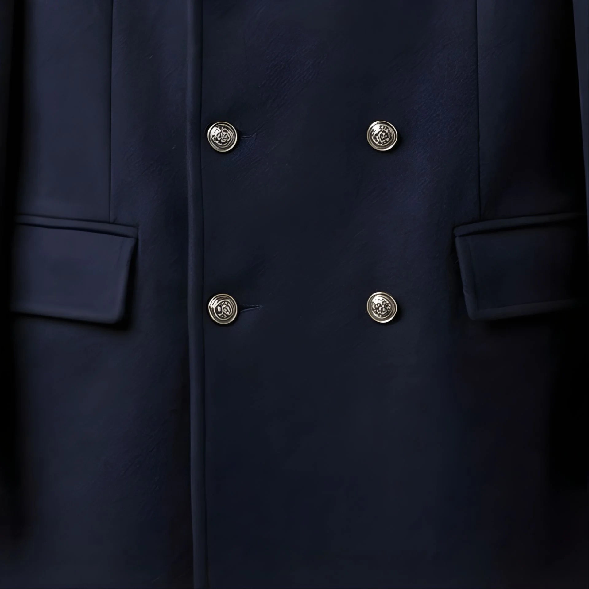 Close up of silver double breasted buttons and flap pockets on men's navy coat.