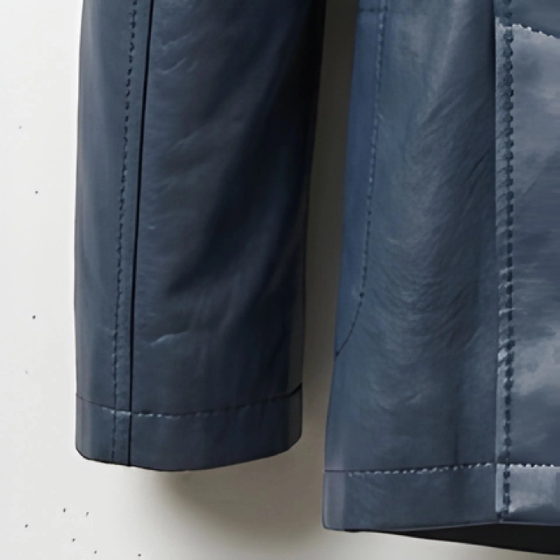 Detail of sleeve cuff and leather texture on men's navy blazer jacket.