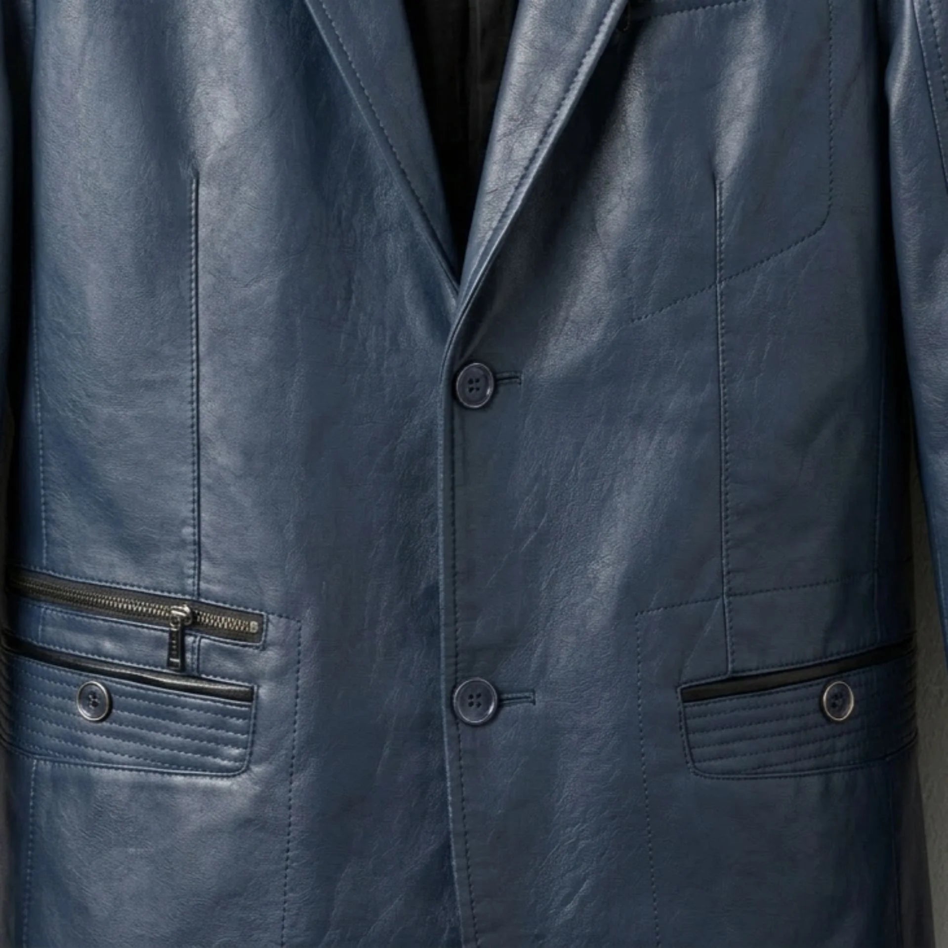 Close up of buttons and zip pockets on men's navy leather blazer.