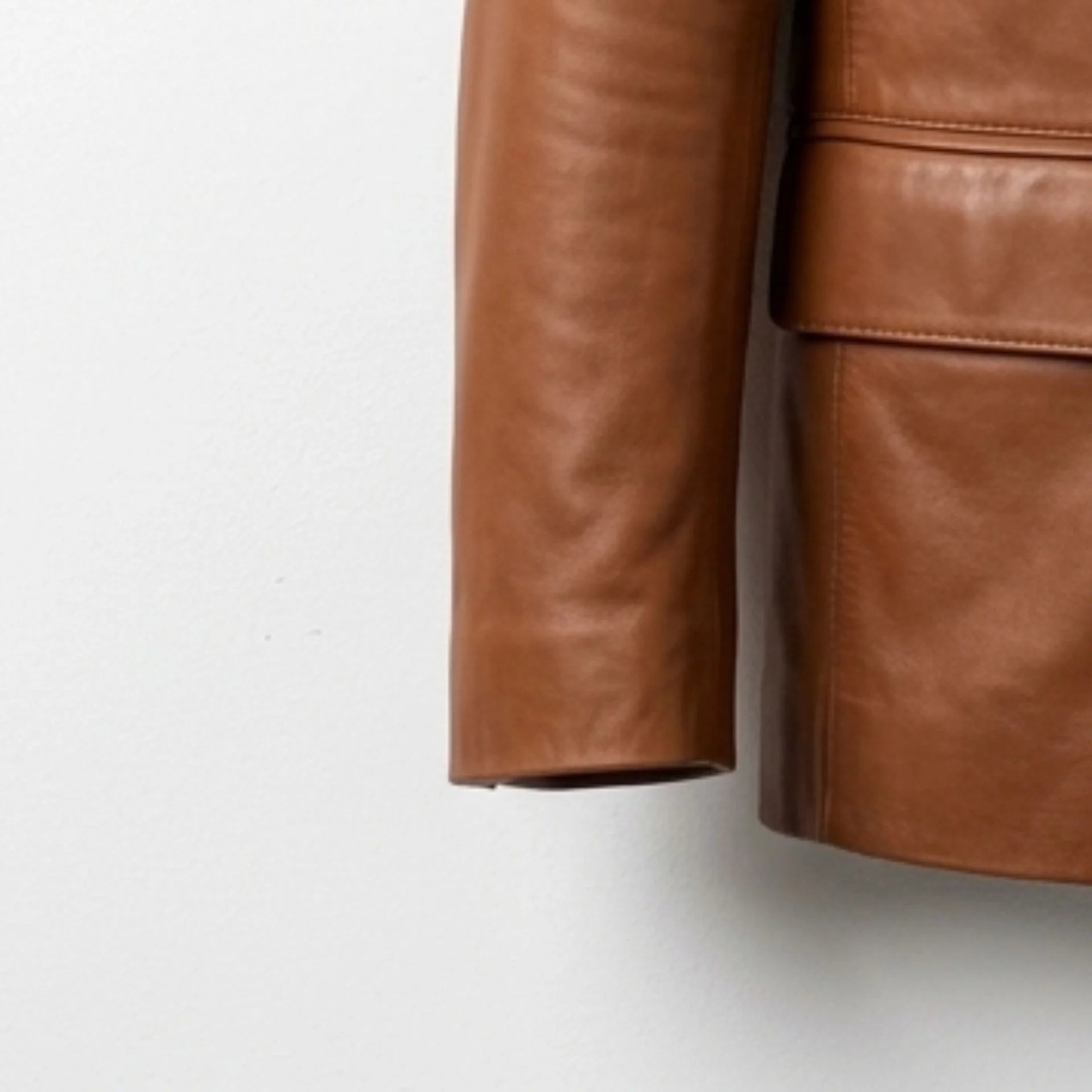 Detail of sleeve and leather texture on men's tan blazer jacket.