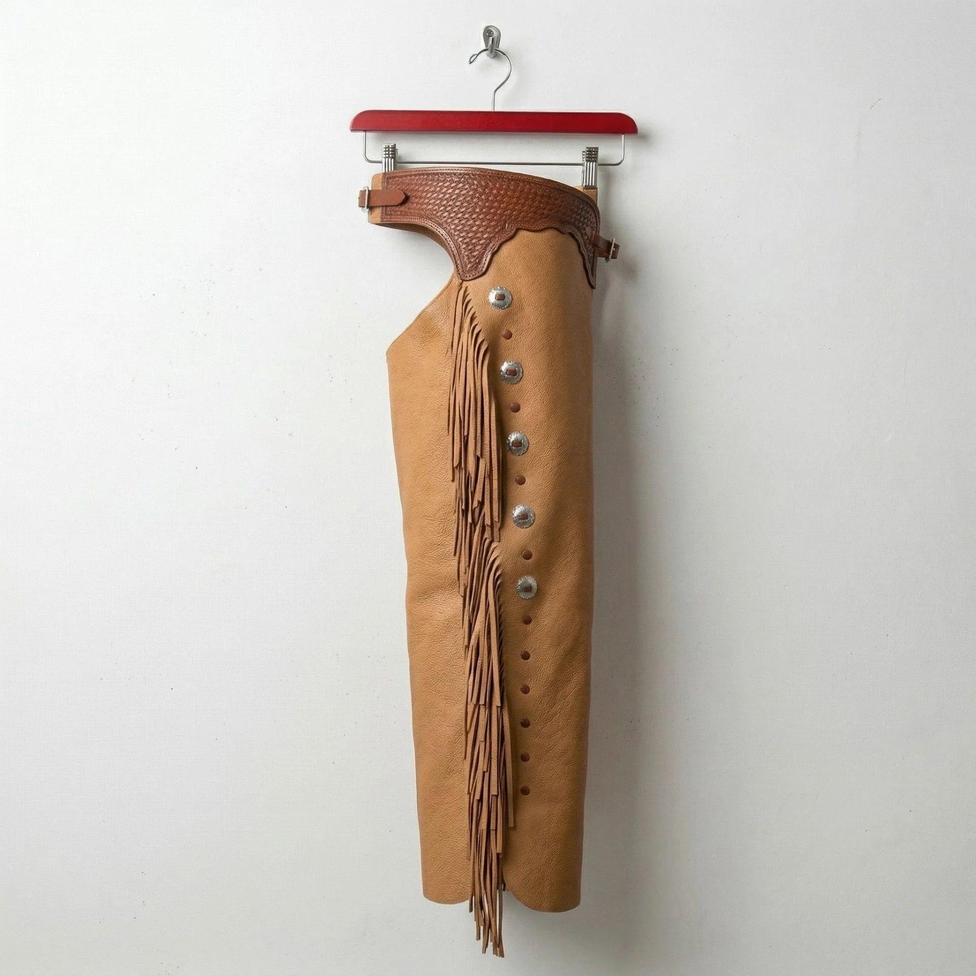 Side profile of tan leather western chaps with fringe and silver conchos