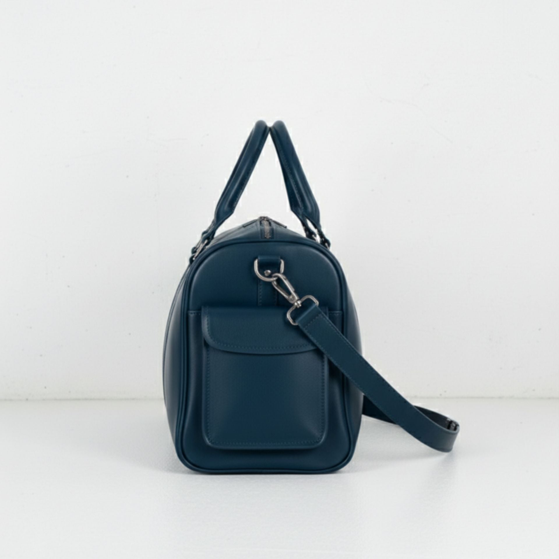 side view navy leather travel duffle with flap pocket and detachable strap.