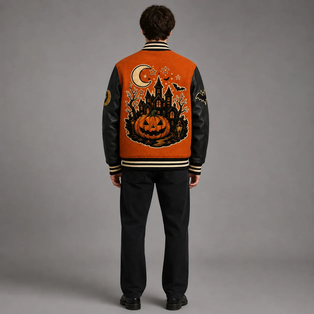 Back studio view of orange and black Halloween varsity jacket showing large haunted castle, pumpkin, moon and bat embroidery