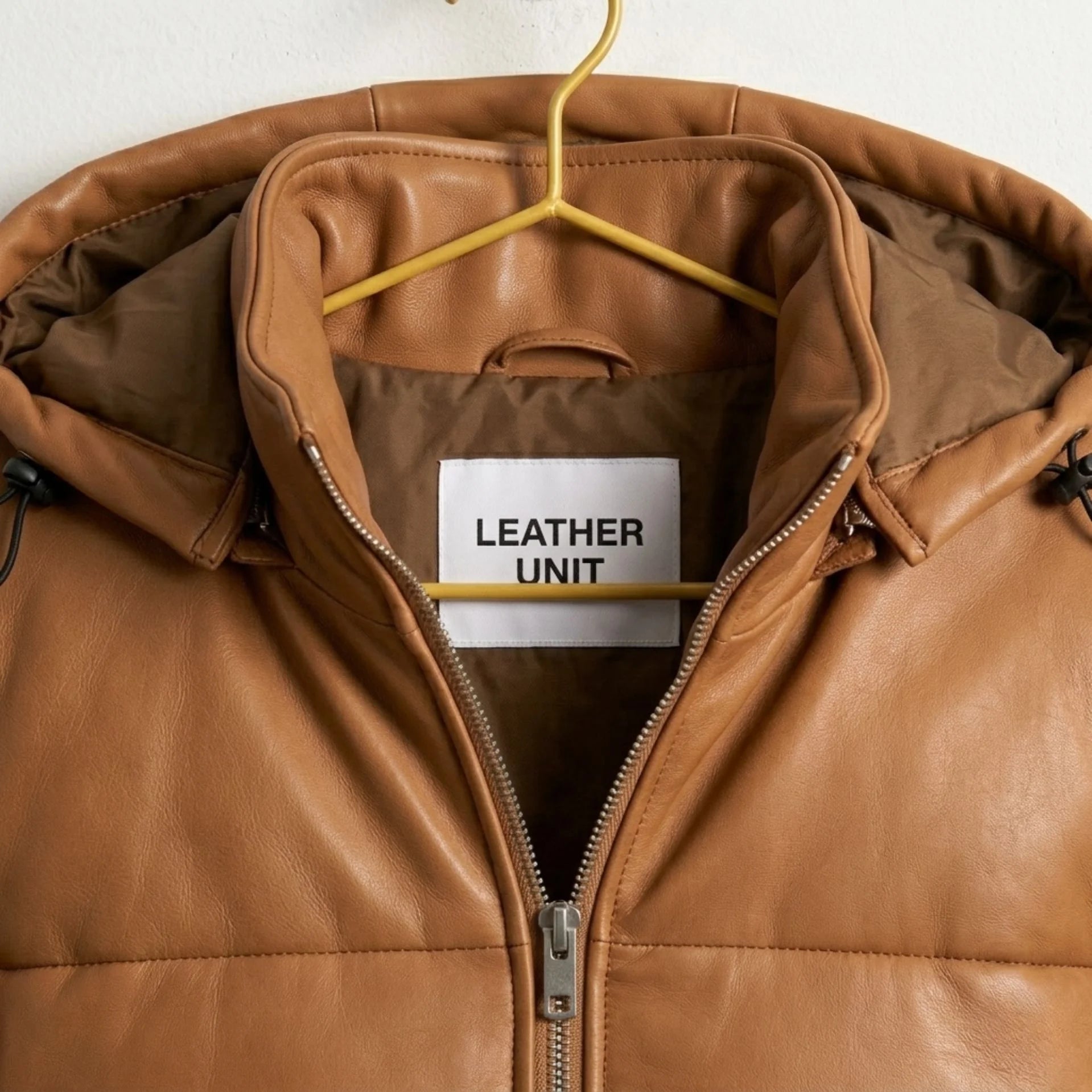 Close-up of hood, collar and Leather Unit branding on tan leather puffer jacket