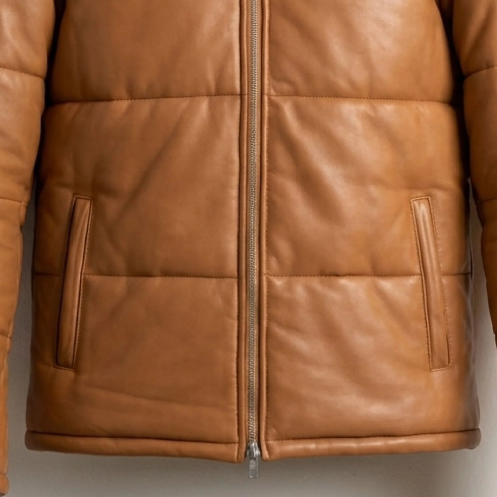 Close-up of front pockets and heavy-duty zipper on tan hooded leather puffer jacket