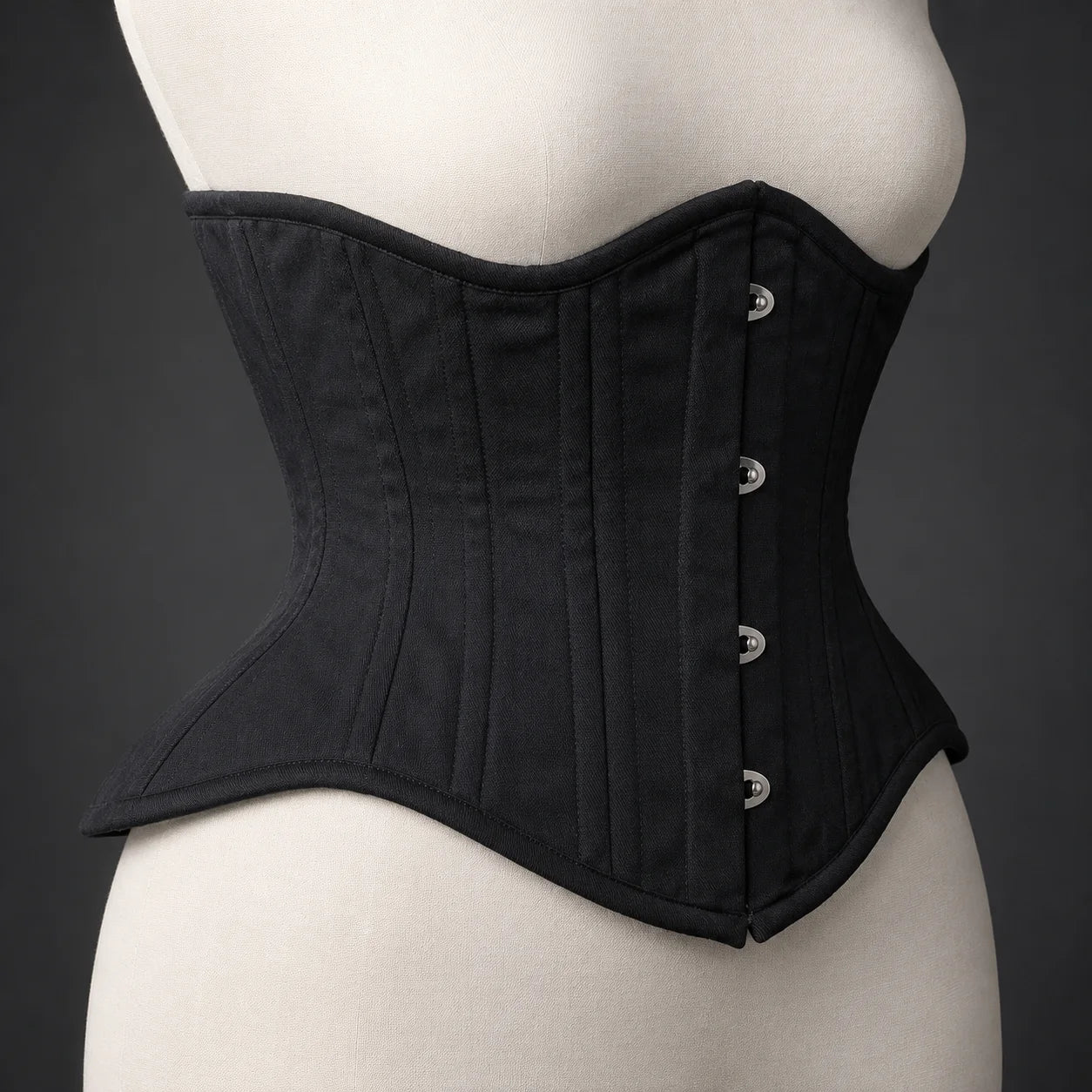 Side profile of black underbust corset showing structured waist shaping, curved upper edge and flared lower panels