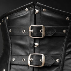 Close-up of black cowhide leather corset showing twin buckle hardware, studs, eyelets, stitching and leather texture.