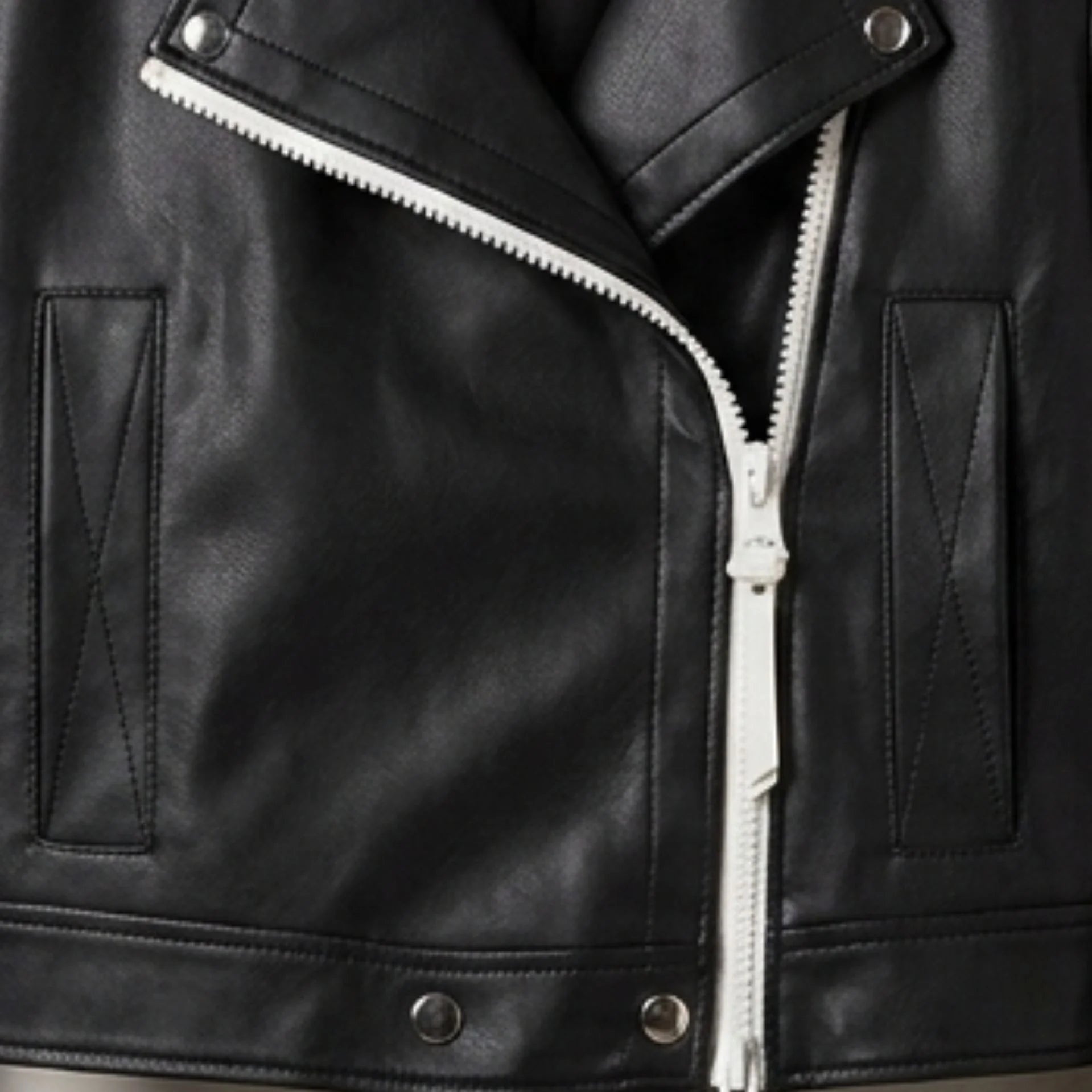 Close-up of white asymmetrical zipper and hem snaps on women’s black moto jacket