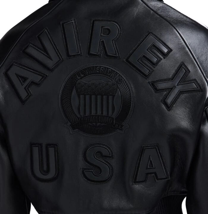 Close-up back view of black cropped leather bomber showing tonal oversized lettering, central crest and USA appliqué