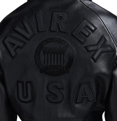 Close-up back view of black cropped leather bomber showing tonal oversized lettering, central crest and USA appliqué