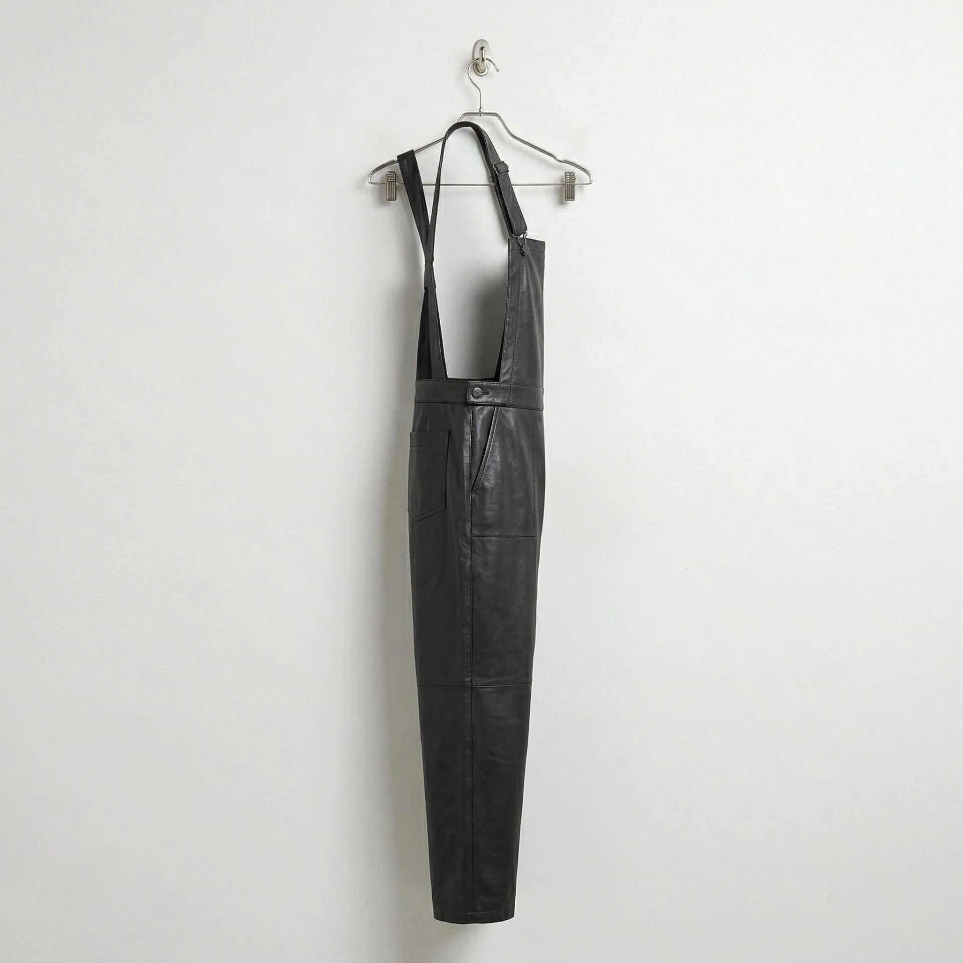 Side profile of black leather bib overalls hanging on hanger