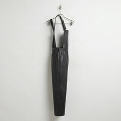 Side profile of black leather bib overalls hanging on hanger