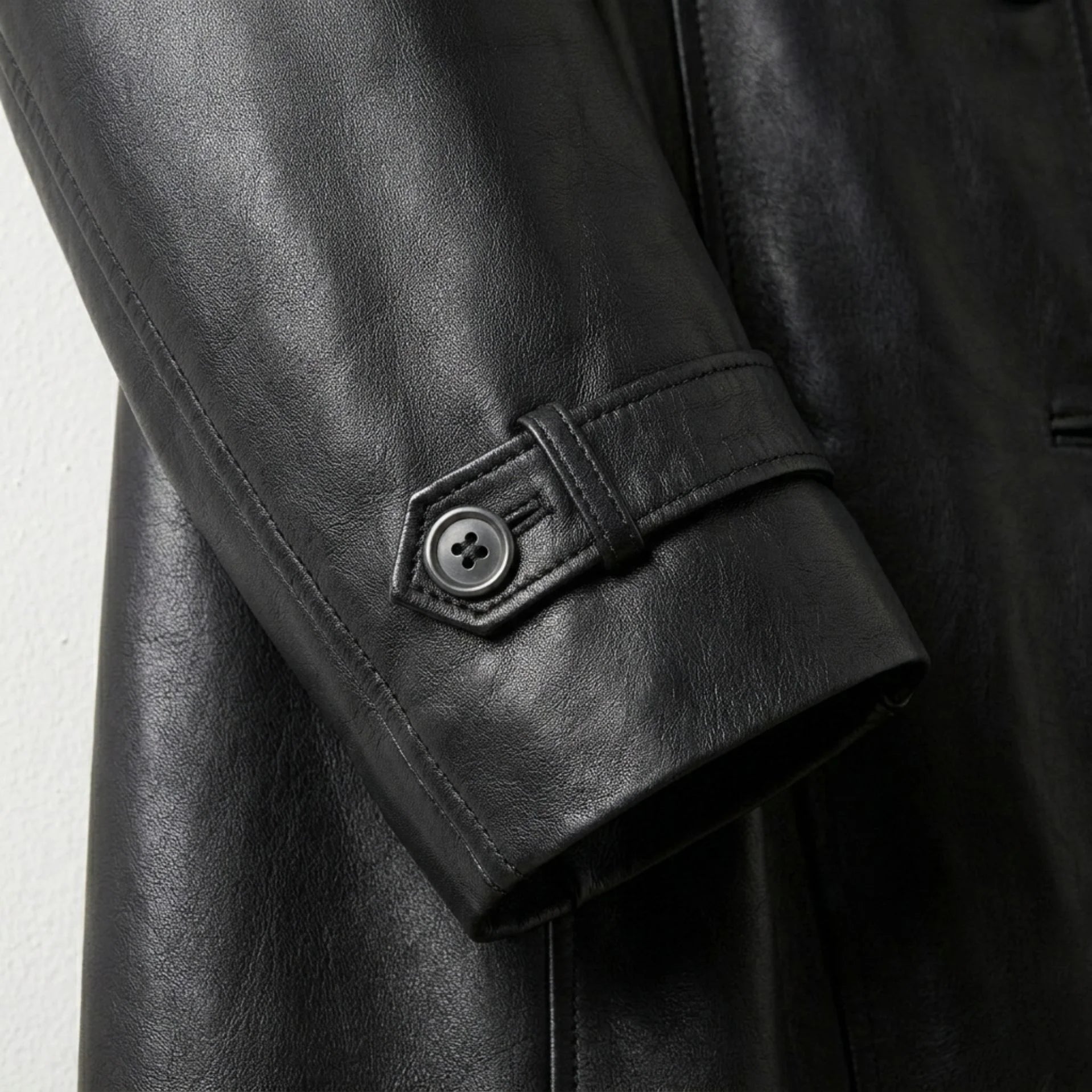 Close up of button tab cuff detail on women’s black leather trench coat