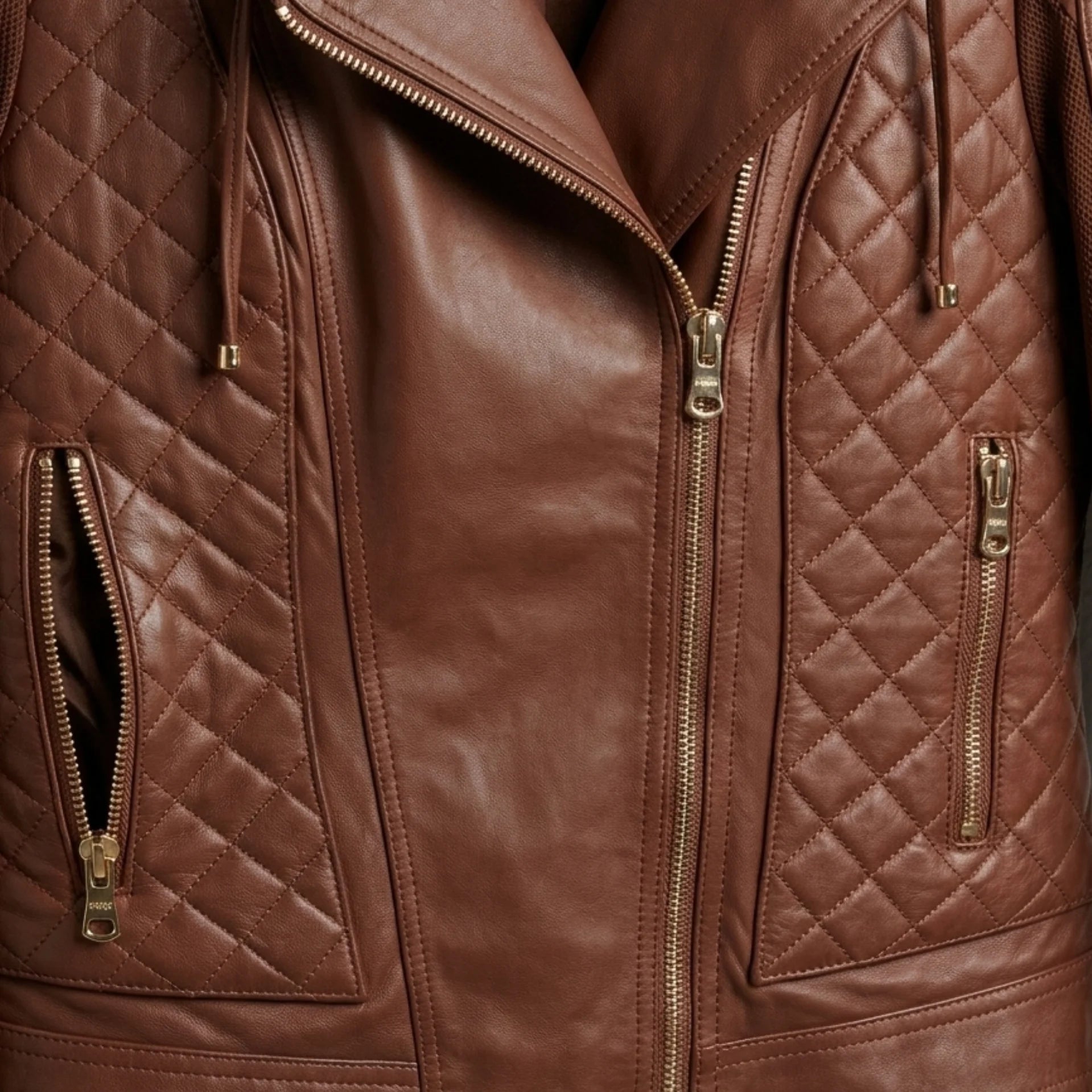 Close-up of front zippers and diamond-quilted panels on women’s brown hooded moto leather jacket.