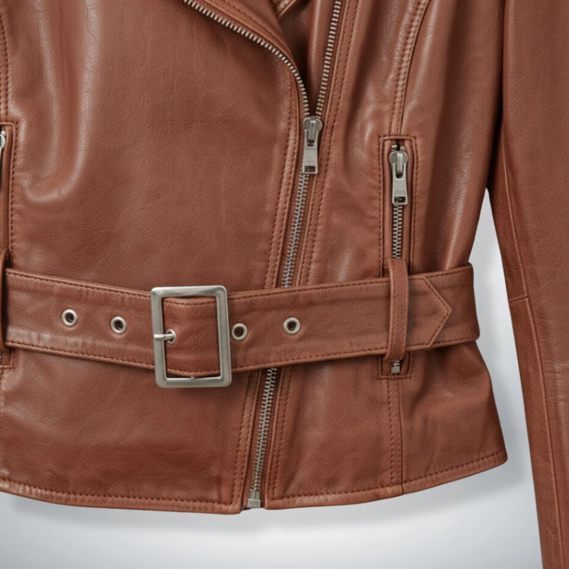 close up of belt and zipper pockets on women's brown leather moto jacket.
