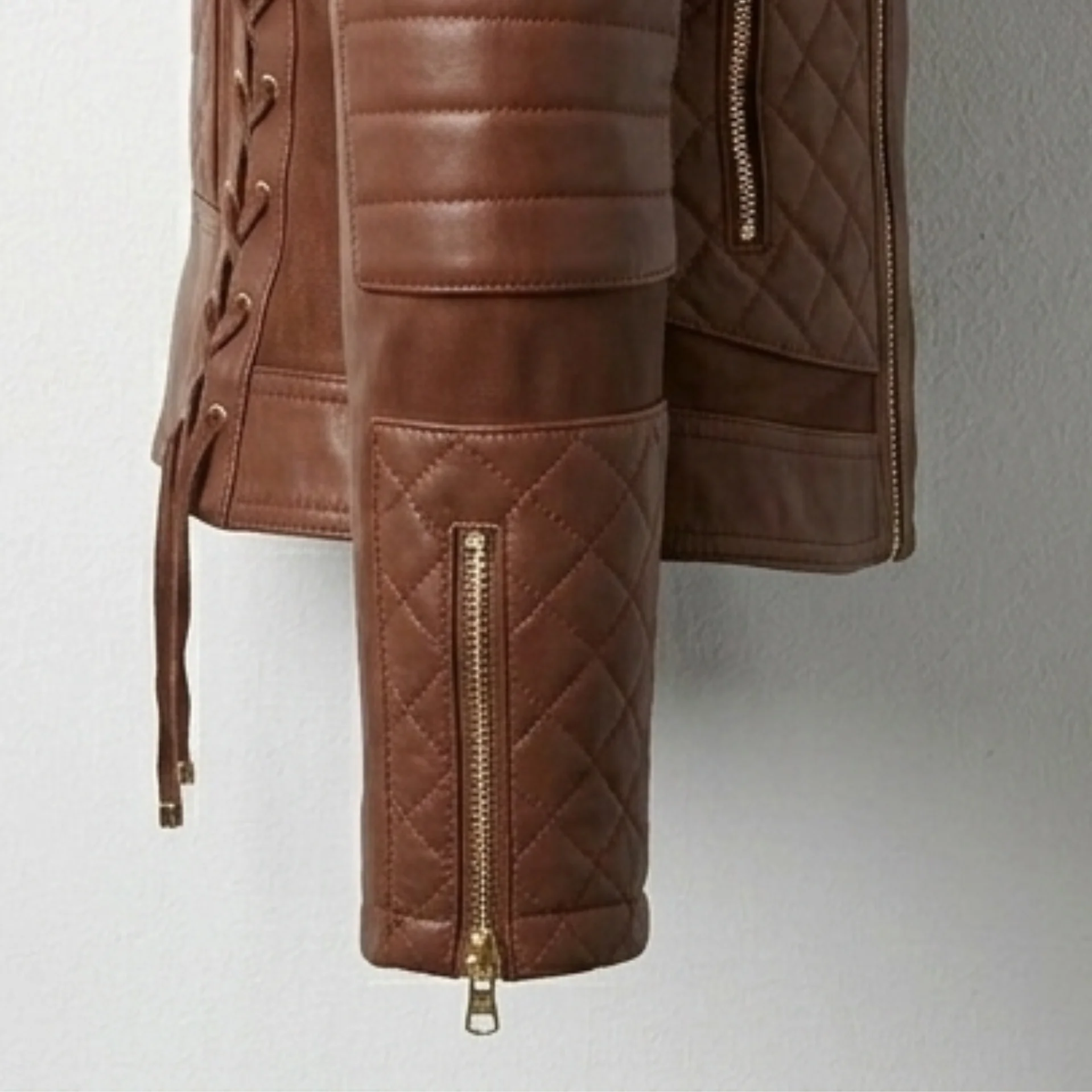 Detail of quilted sleeve, padded elbow and cuff zipper on women’s brown hooded moto leather biker jacket.