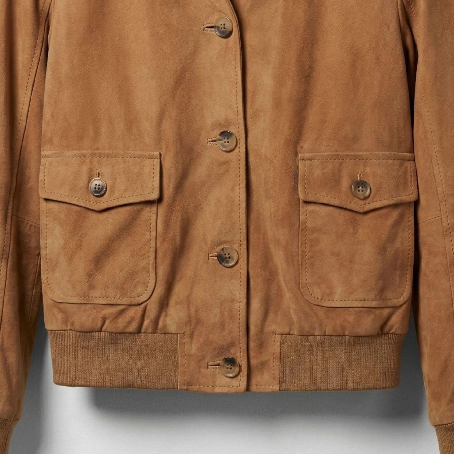 Close-up of buttoned flap pockets and ribbed hem on women’s suede bomber