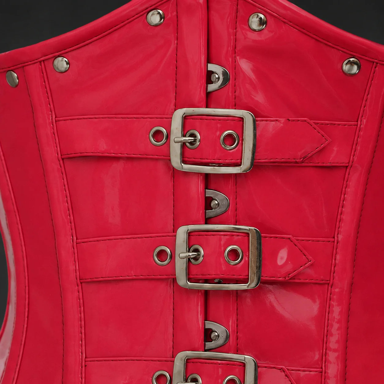 Close-up of pink PVC corset front showing glossy texture, buckle straps, stitching, eyelets and rivet details