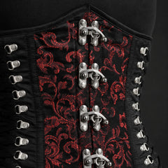 Close-up of red brocade corset front showing ornamental textile pattern, metal clasp hardware and side lacing