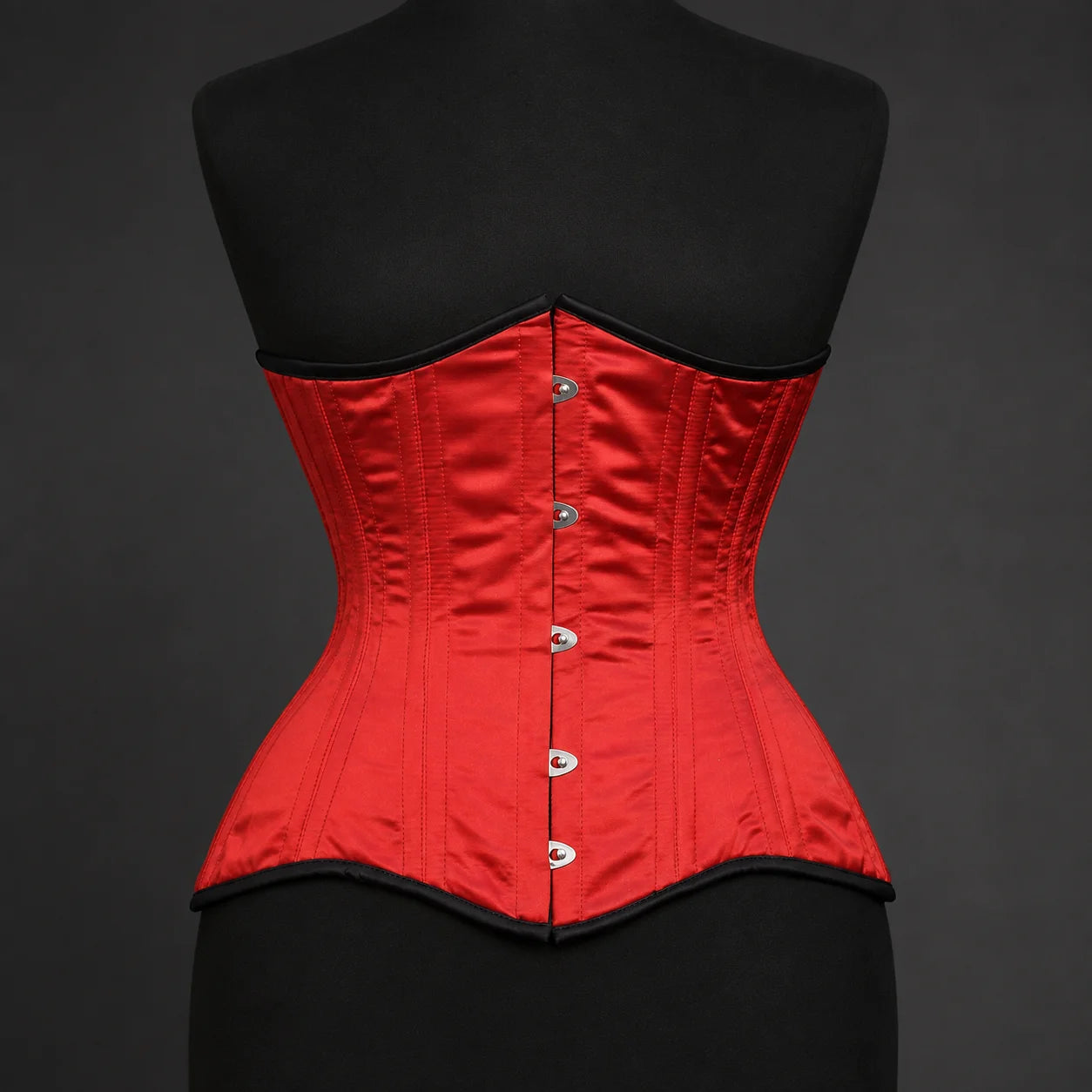 Front studio view of red satin underbust corset showing vertical boning channels and busk-style fastening